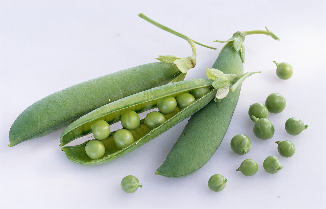 Three pea pods and single peas on a light background