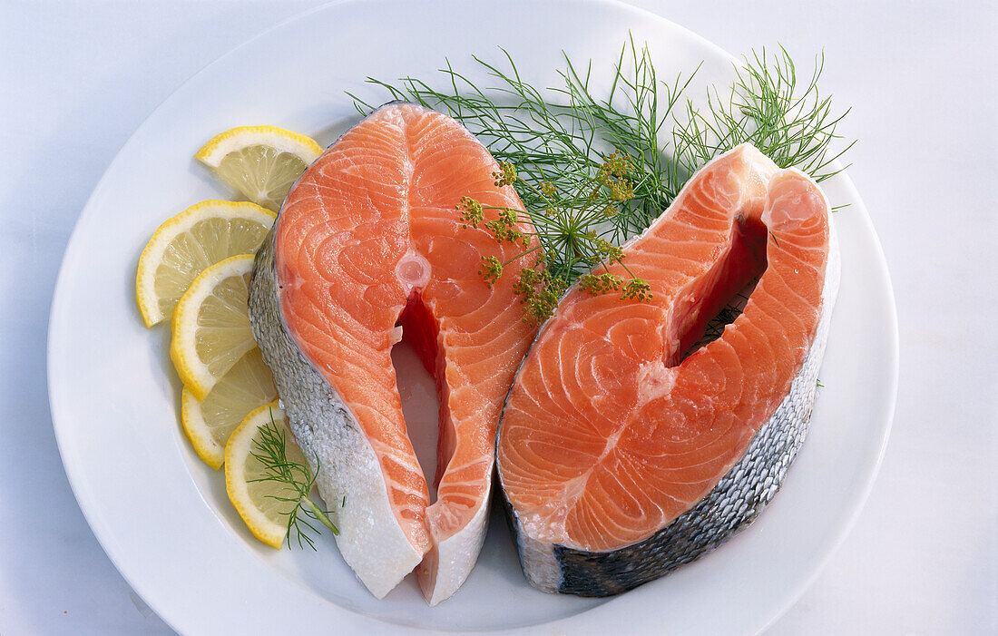 Two salmon steaks, lemon, and dill on a white plate