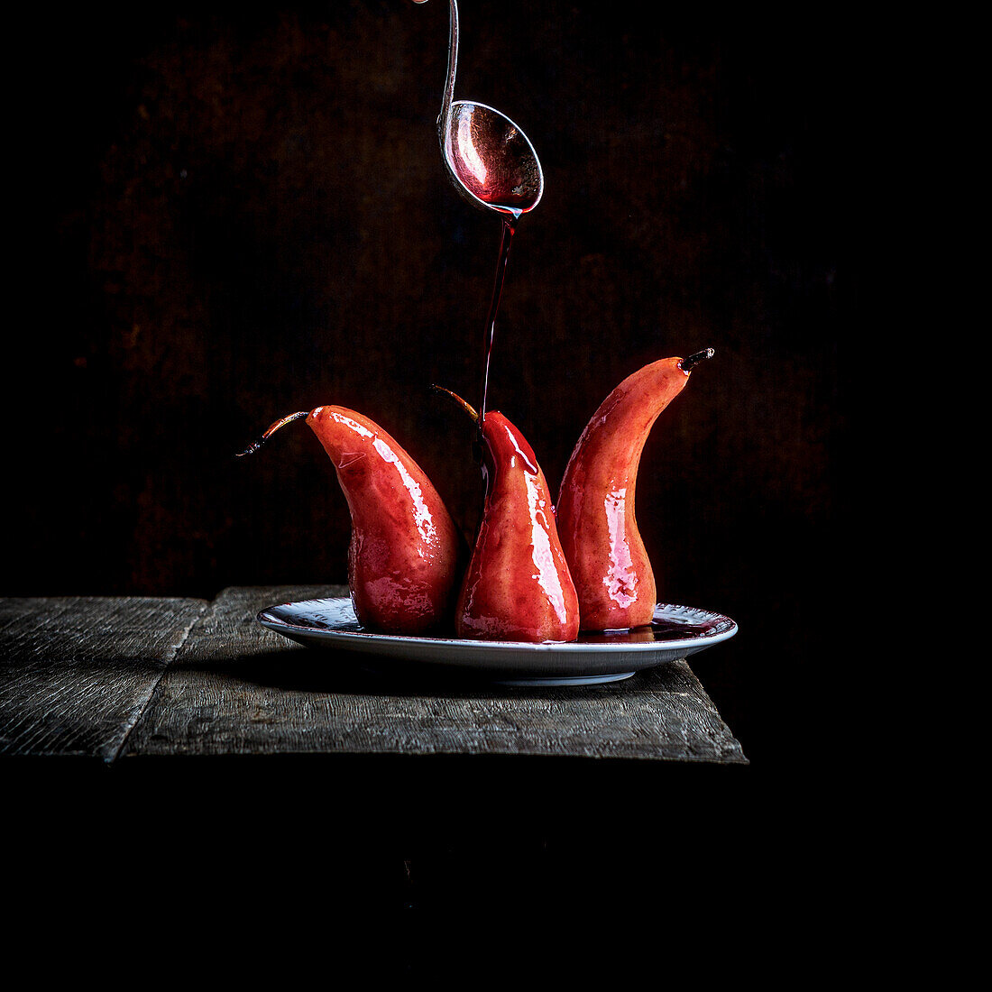 Pochierte Birnen mit Rotweinsauce auf Holztisch vor schwarzem Hintergrund