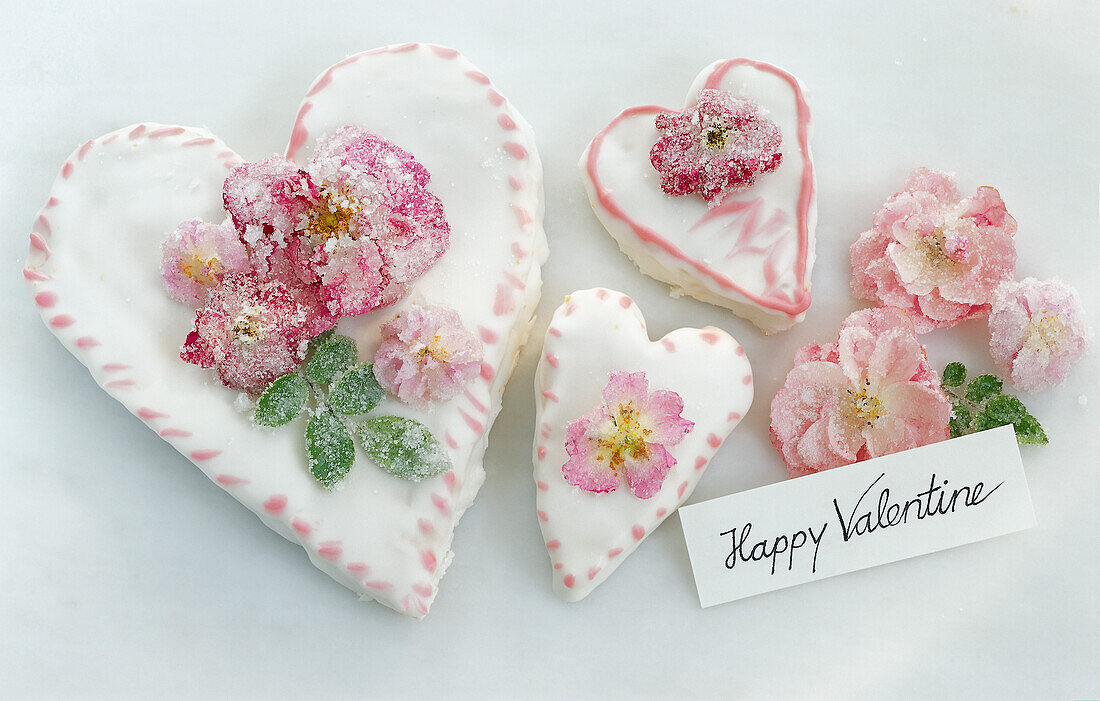 Drei herzförmige Torten zum Valentinstag, mit gezuckerten Rosenblüten