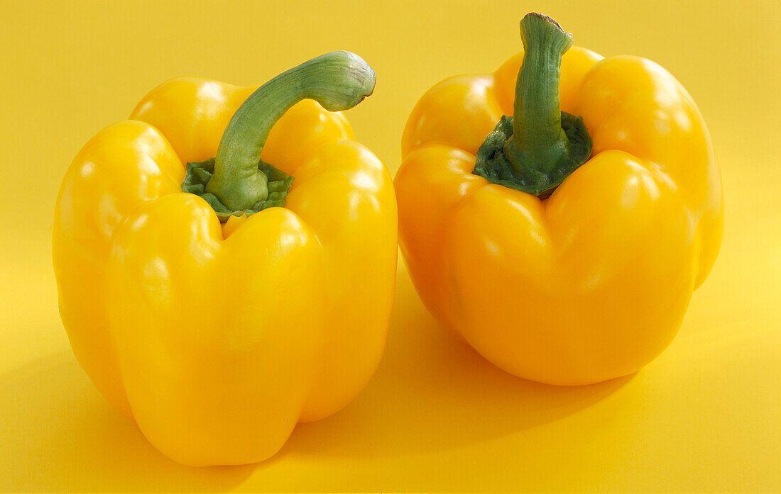 Two yellow peppers on a yellow background
