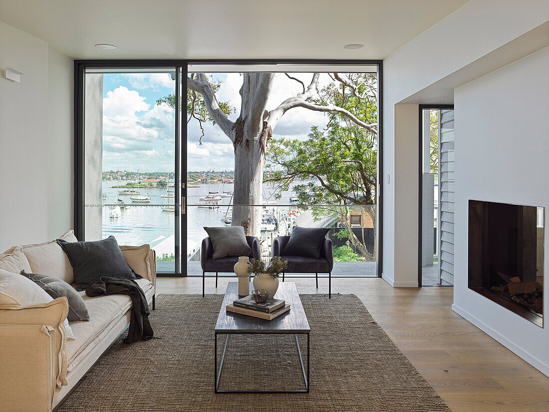 Wohnzimmer mit hellem Sofa und Kamin und mit Blick auf das Wasser