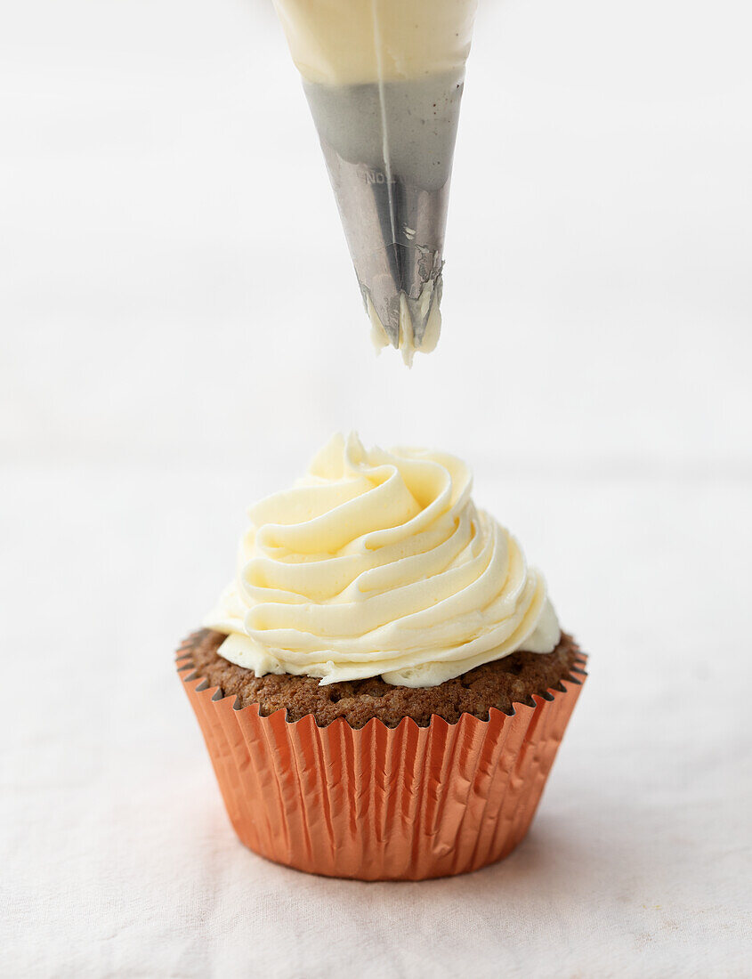 Piping buttercream onto a chai cupcake