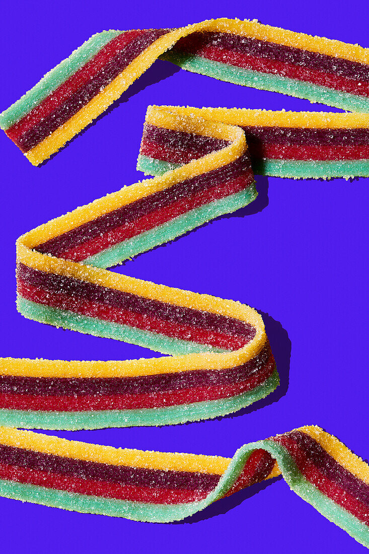 Sour fruit jelly strips sprinkled with sugar on a coloured background