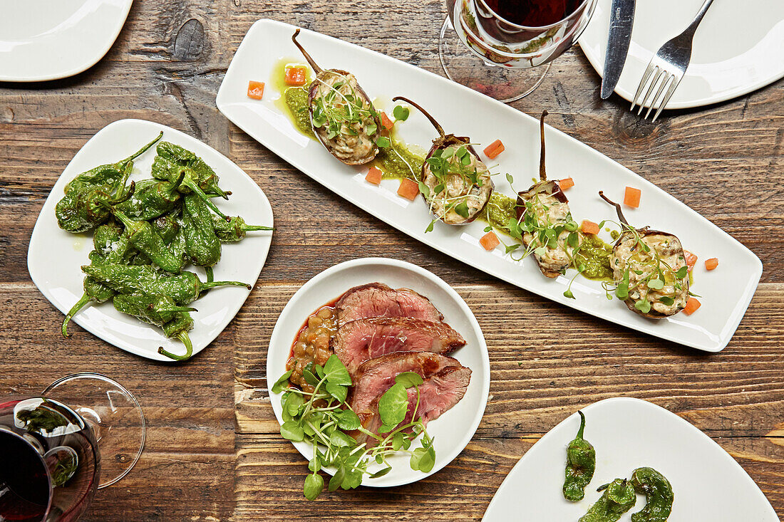 Plates of Spanish tapas. Padron peppers, seared beef and stuffed aubergines