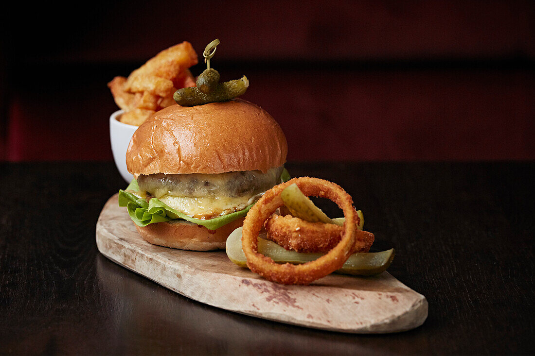 Cheeseburger im Briochebrötchen mit Zwiebelringen, Gurken und Cornichons