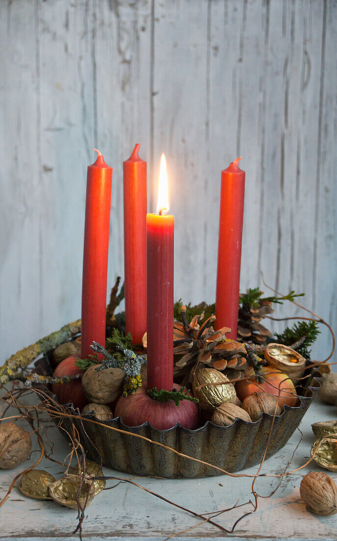 Backform gefüllt mit Kerzen in Äpfel gesteckt, vergoldete Walnüsse und Eicheln