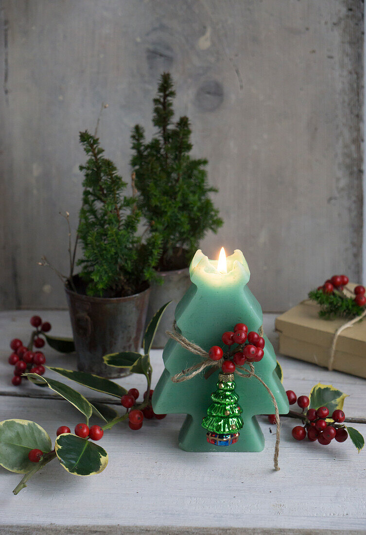 Kerze in Tannenbaum Form, dekoriert mit Ilexbeeren und Christbaumanhänger