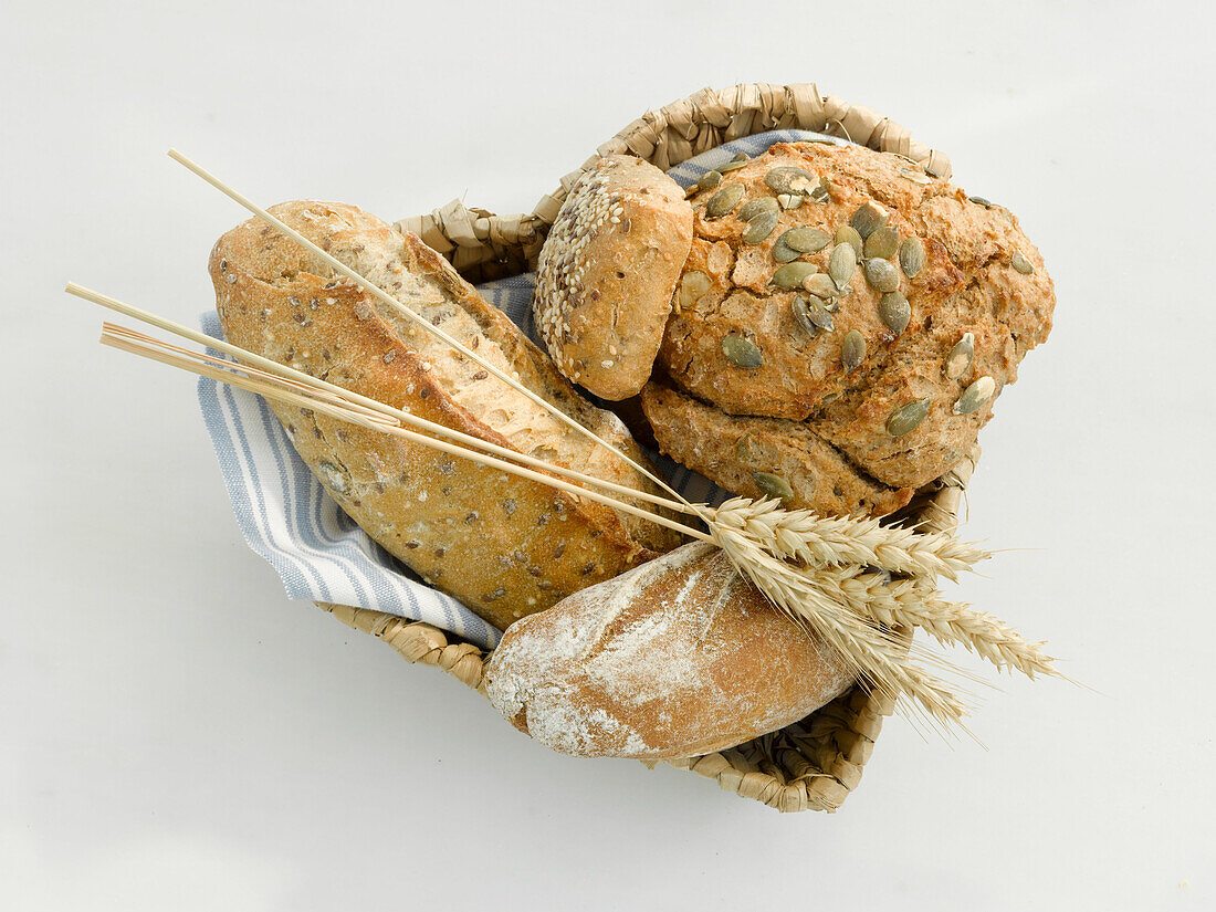 Ein herzförmiges Körbchen mit Brötchen und Ähren auf hellem Untergrund