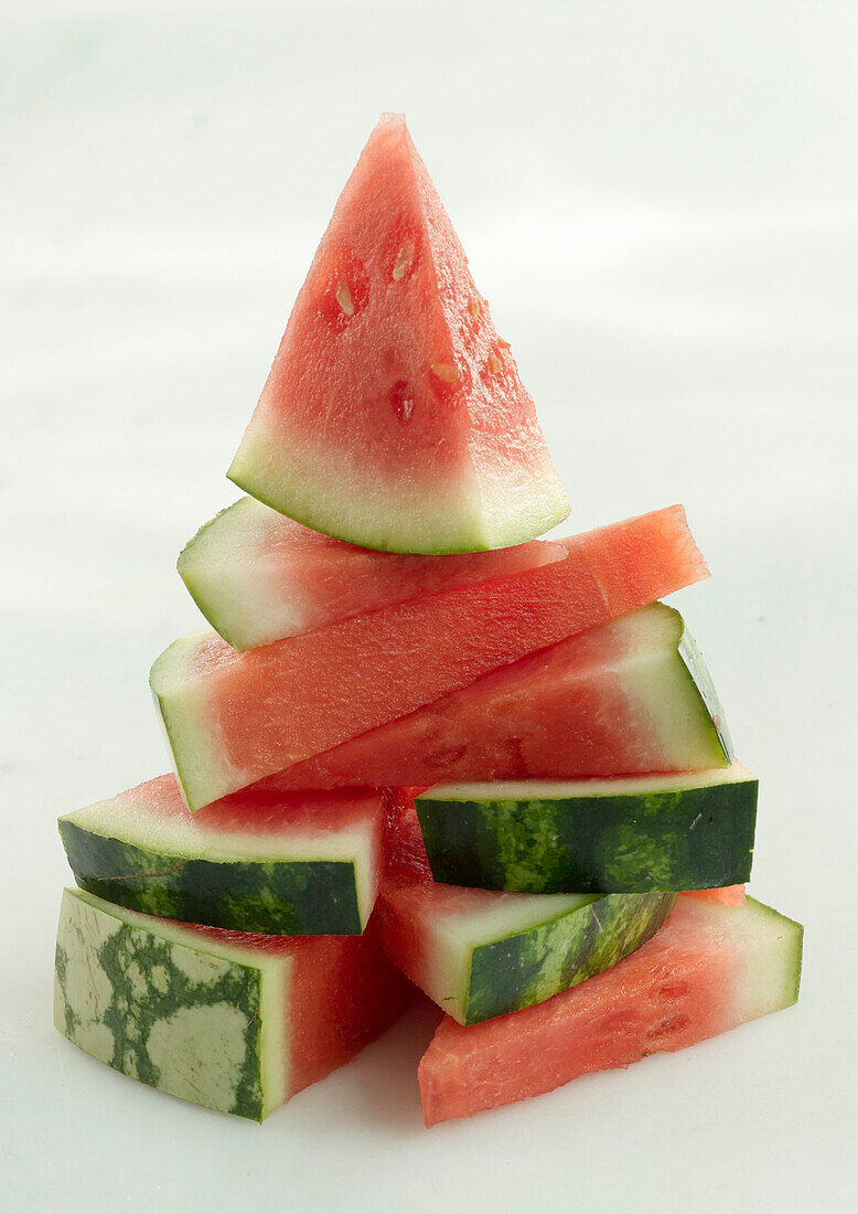 Pile of watermelon slices cut into triangles on a light background