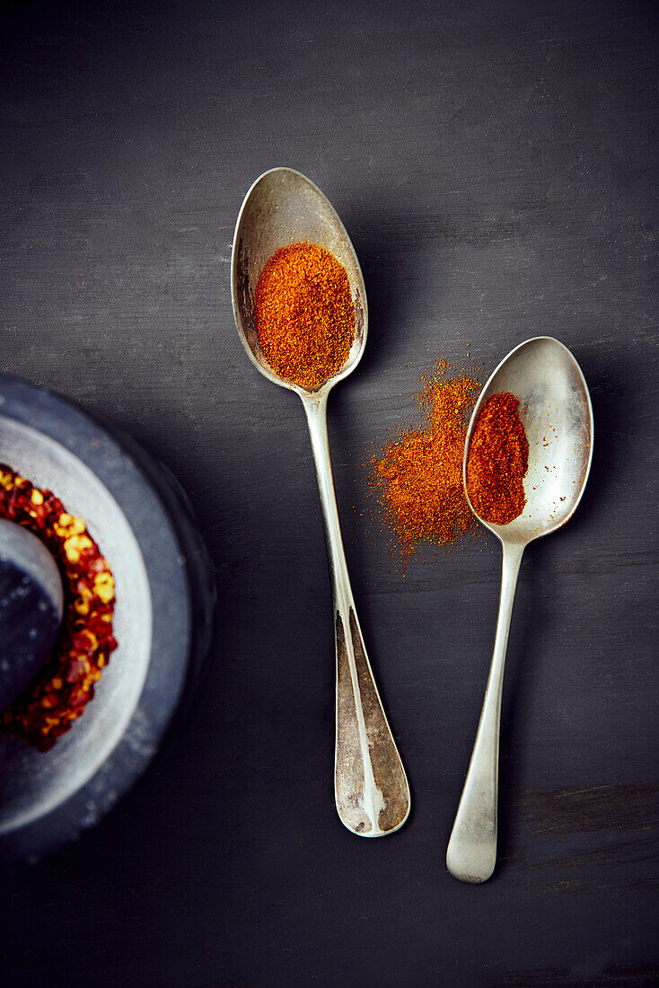 Paprika spice on two spoons and chili flakes in a mortar