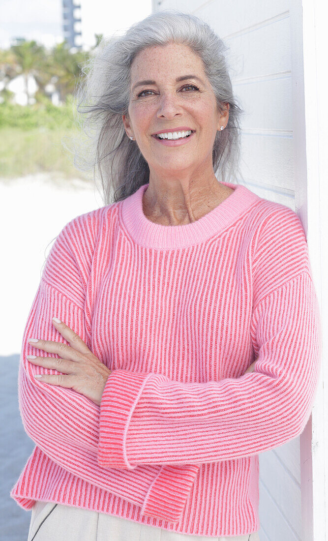 Gray haired woman in a pink sweater on the beach