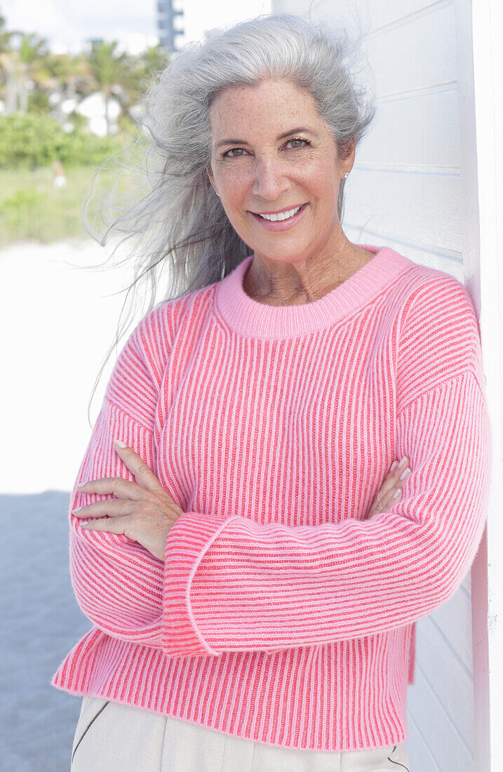 Grauhaarige Frau in pinkfarbenem Pullover am Strand