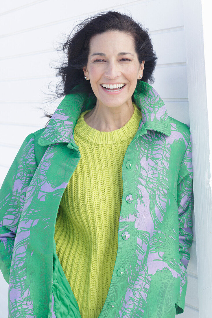 Mature, dark-haired woman in a green coat and green and yellow knit sweater