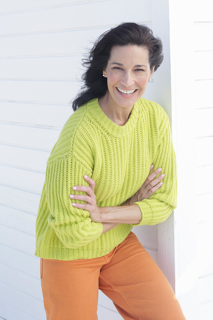 Reife, dunkelhaarige Frau in grüngelbem Strickpullover und orangefarbener Hose