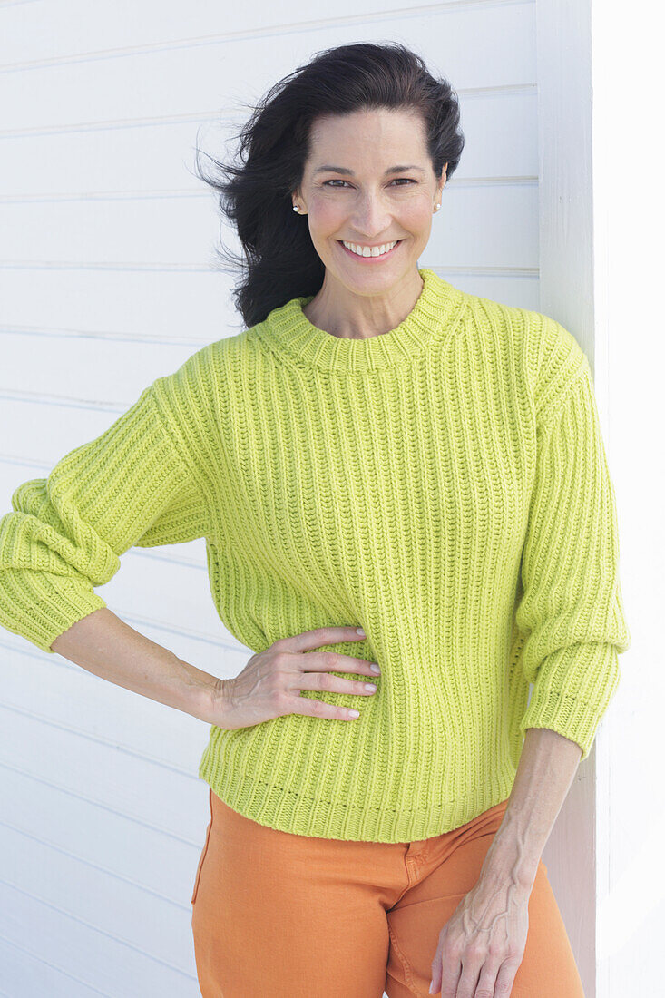 Mature, dark-haired woman in a green and yellow knit sweater and orange pants