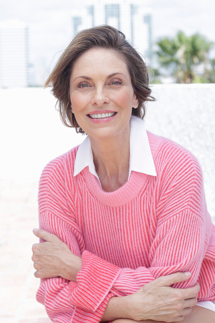 Frau in pinkfarbenem Pullover und weißem Hemd am Strand