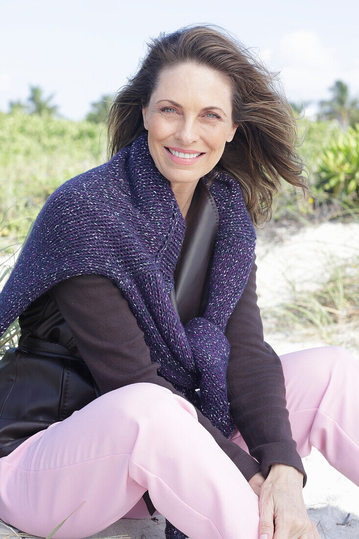 Long-haired woman in a dark coat with a sweater over her shoulders on the beach