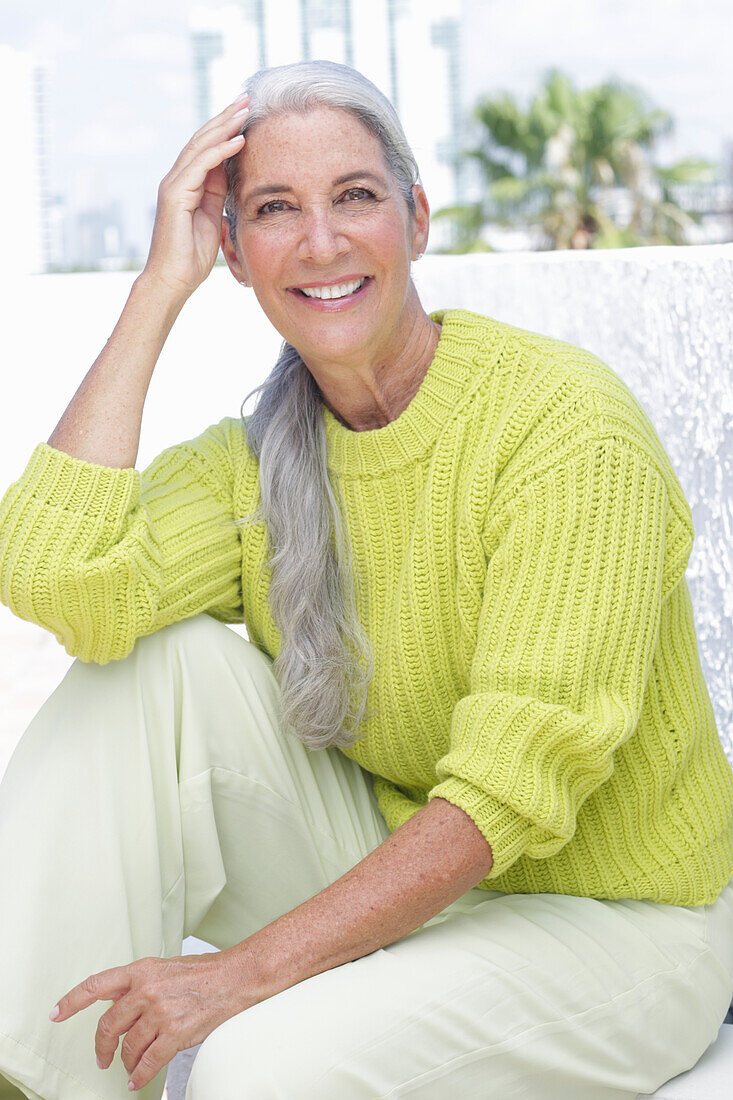 Grauhaarige Frau in grüngelbem Strickpullover und heller Hose