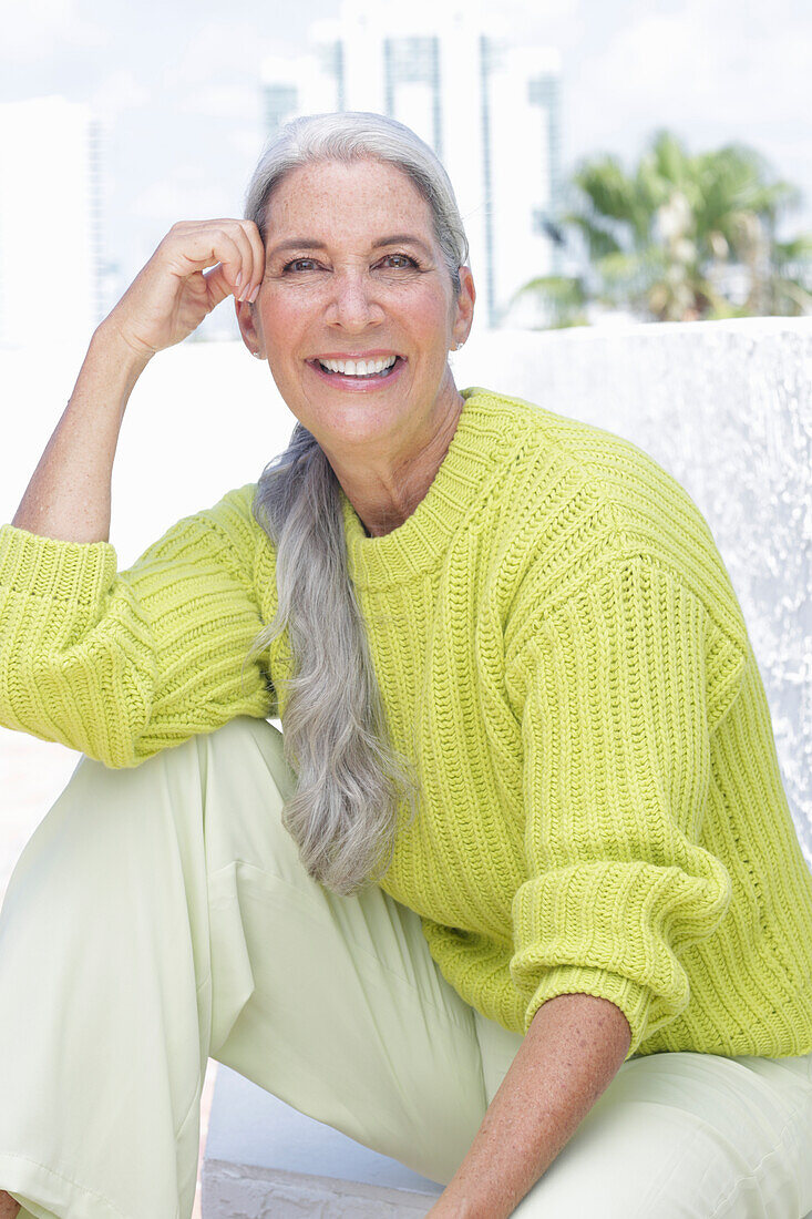 Gray-haired woman in a green-yellow knit sweater and light-colored trousers