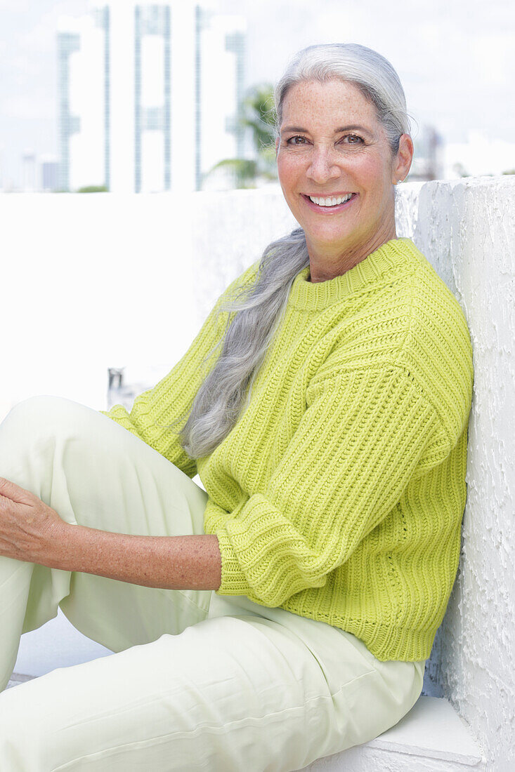 Gray-haired woman in a green-yellow knit sweater and light-colored trousers