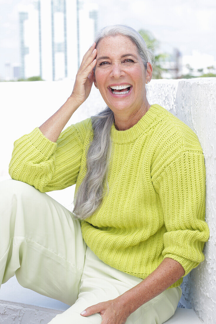 Lachende grauhaarige Frau in grüngelbem Strickpullover und heller Hose
