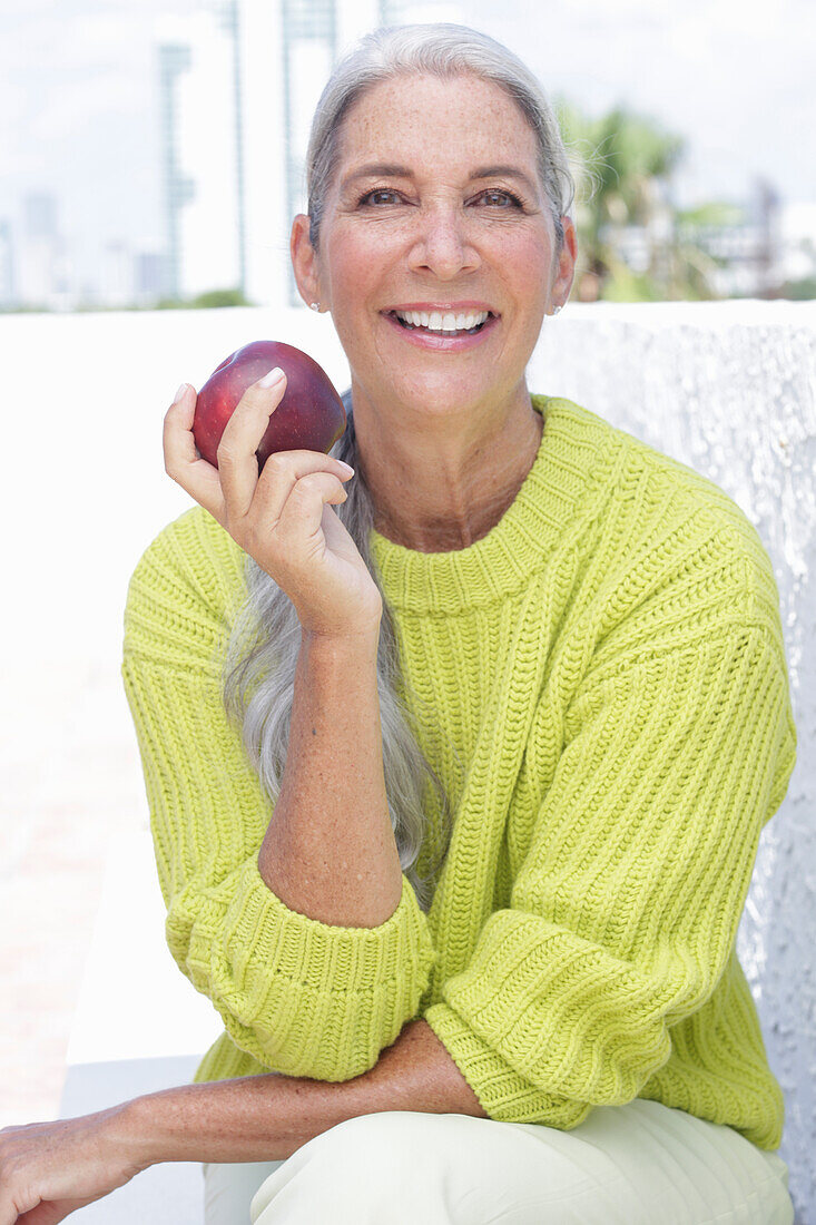 Gray-haired woman with an apple in a green and yellow knit sweater