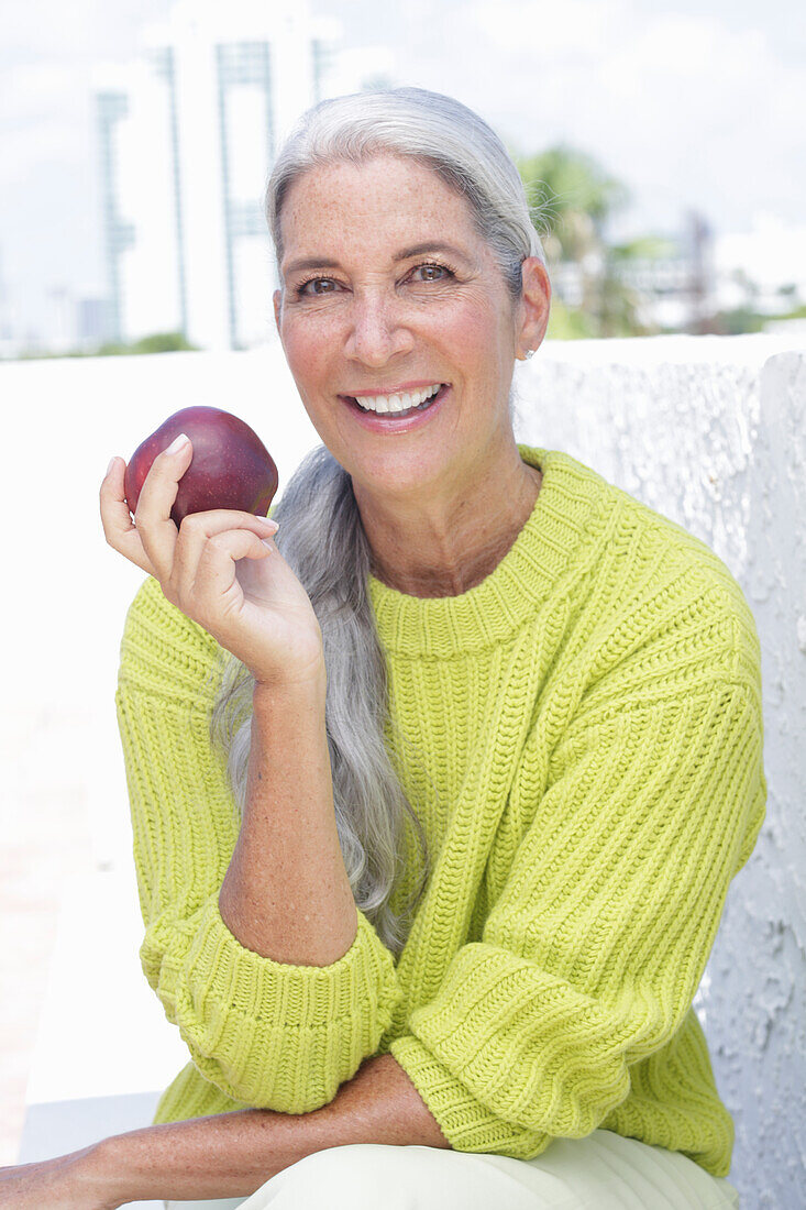 Gray-haired woman with an apple in a green and yellow knit sweater