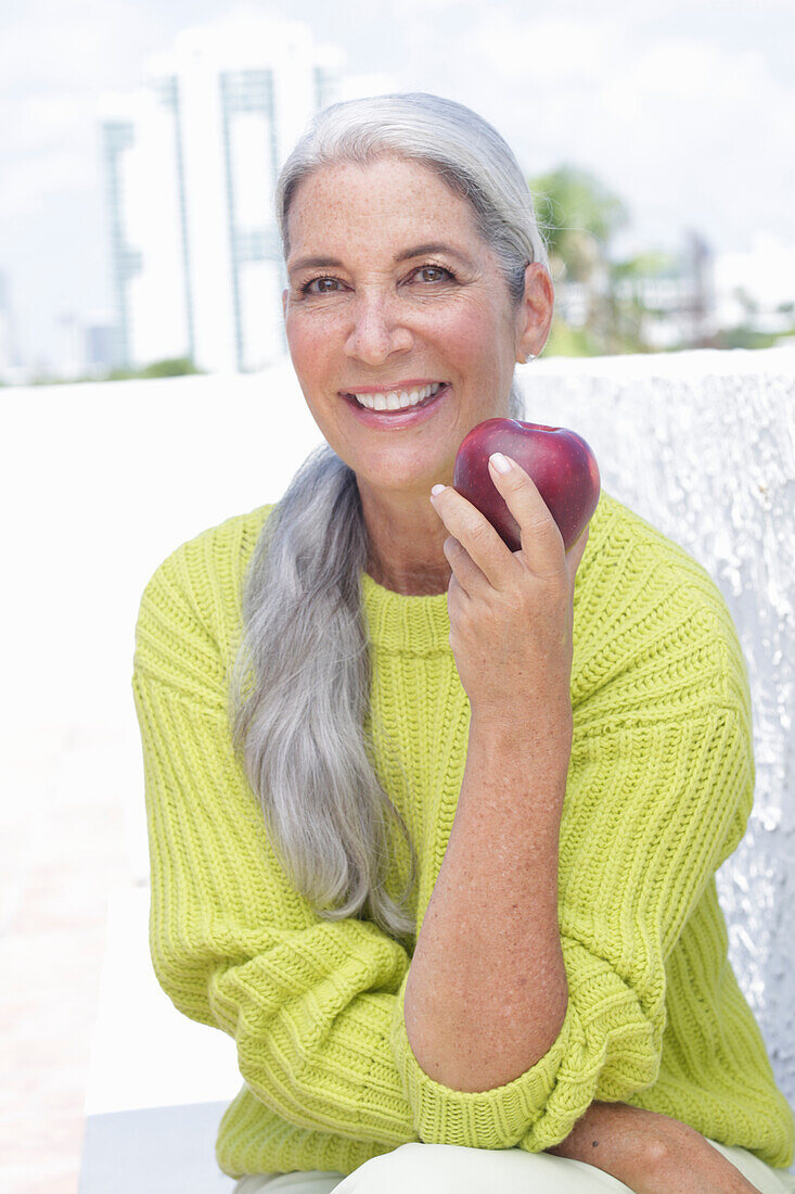 Grauhaarige Frau mit einem Apfel in grüngelbem Strickpullover