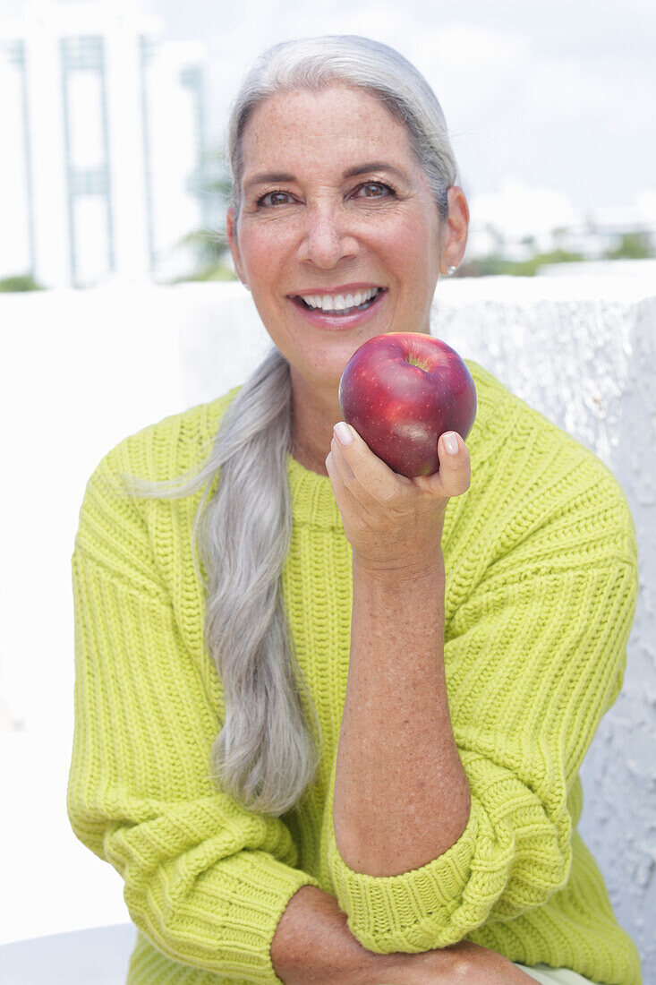 Gray-haired woman with an apple in a green and yellow knit sweater