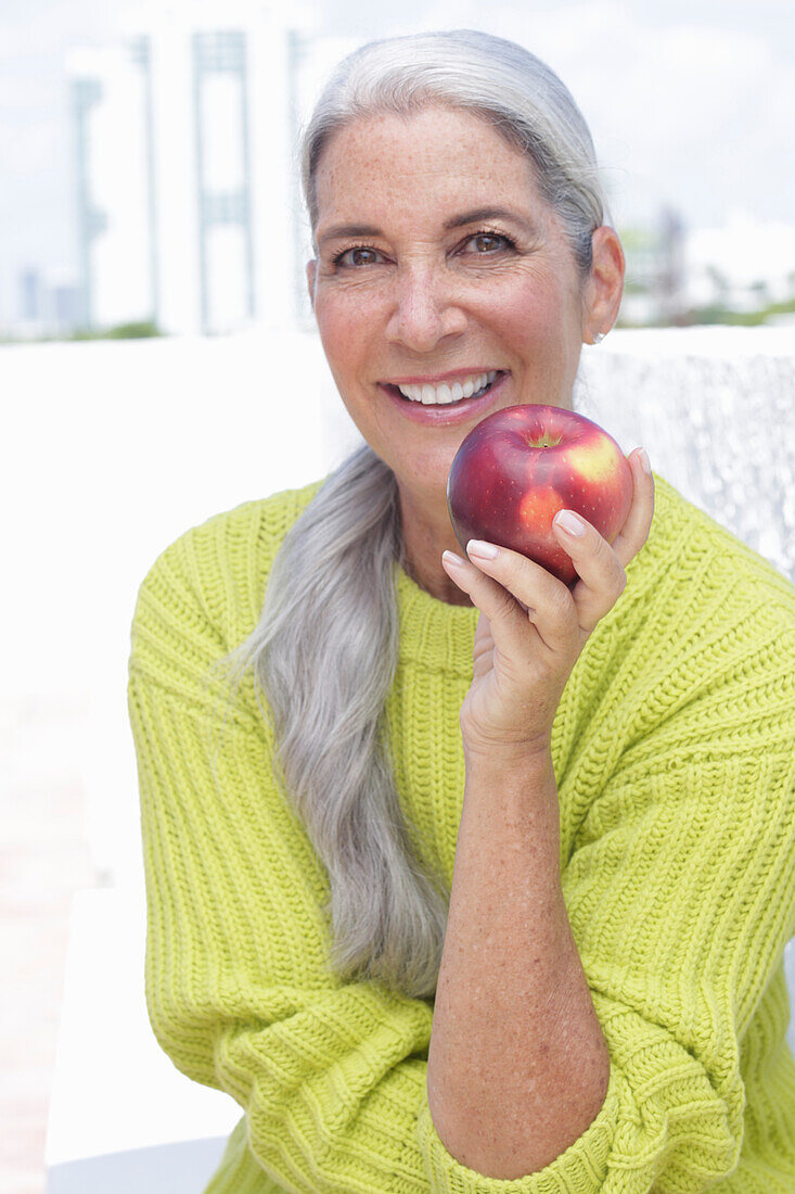 Grauhaarige Frau mit einem Apfel in grüngelbem Strickpullover