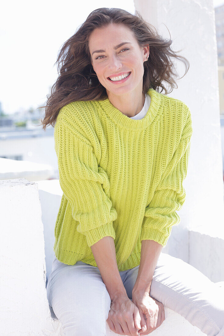 Cheerful longhaired woman in green-yellow knitted jumper and white trousers