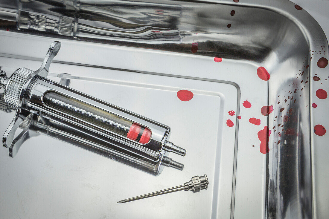 Vintage metal syringe and needle in blood-stained metal tray