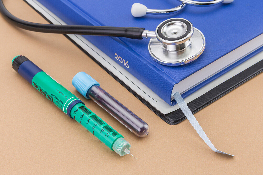 Stethoscope next to a book, insulin pen and blood sample