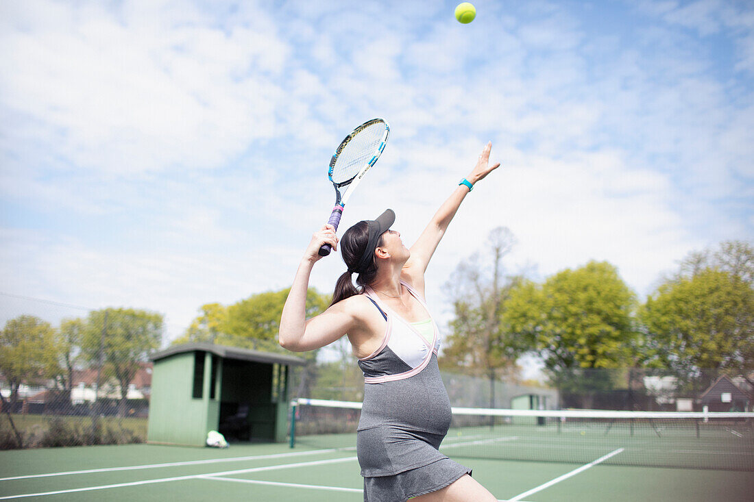 Pregnant woman playing tennis on sunny tennis court