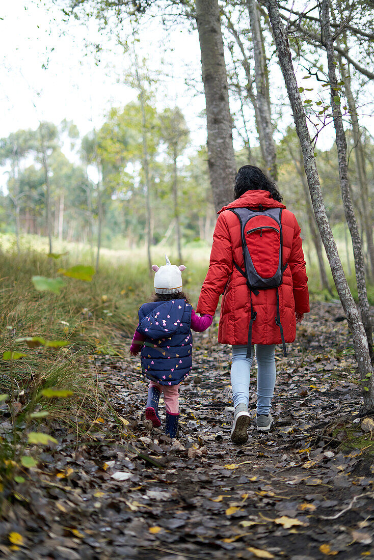 Mother and daughter holding hands walking on trail in woods