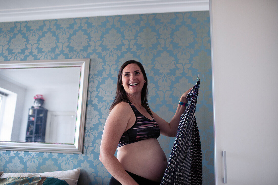 Happy pregnant woman getting dressed at bedroom closet