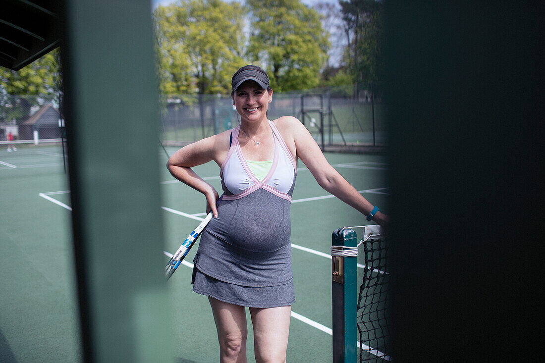 Confident pregnant woman in dress on sunny tennis court