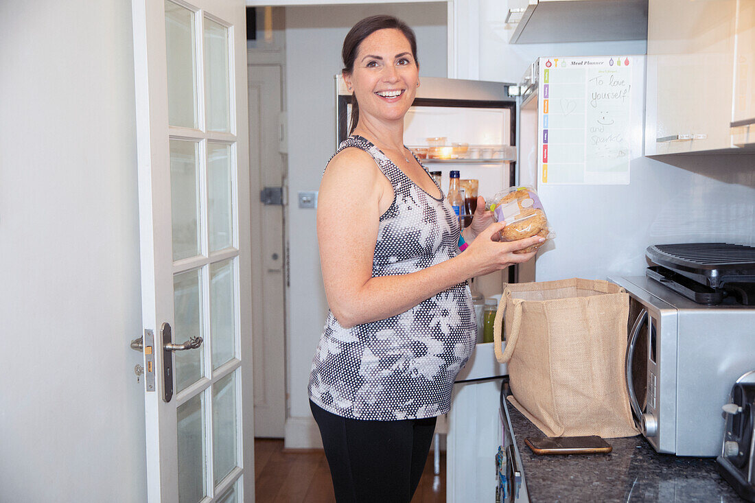Happy pregnant woman putting away groceries in kitchen