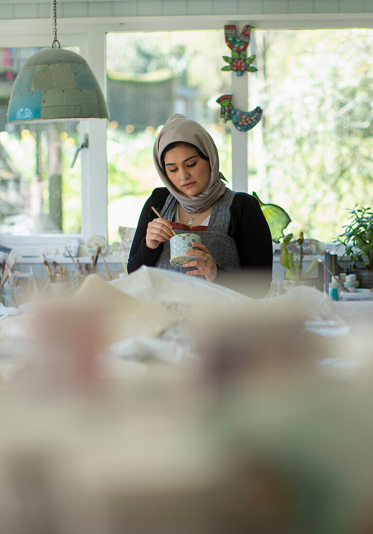 Young female artist in hijab painting ceramics in art studio