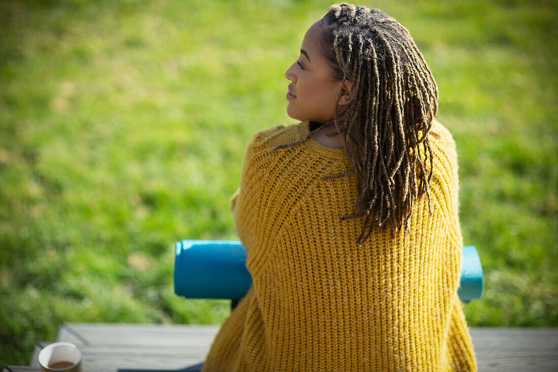 Young woman in sweater with yoga mat on sunny patio