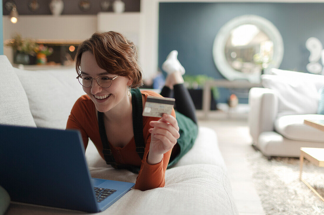 Happy woman with credit card online shopping at laptop on sofa