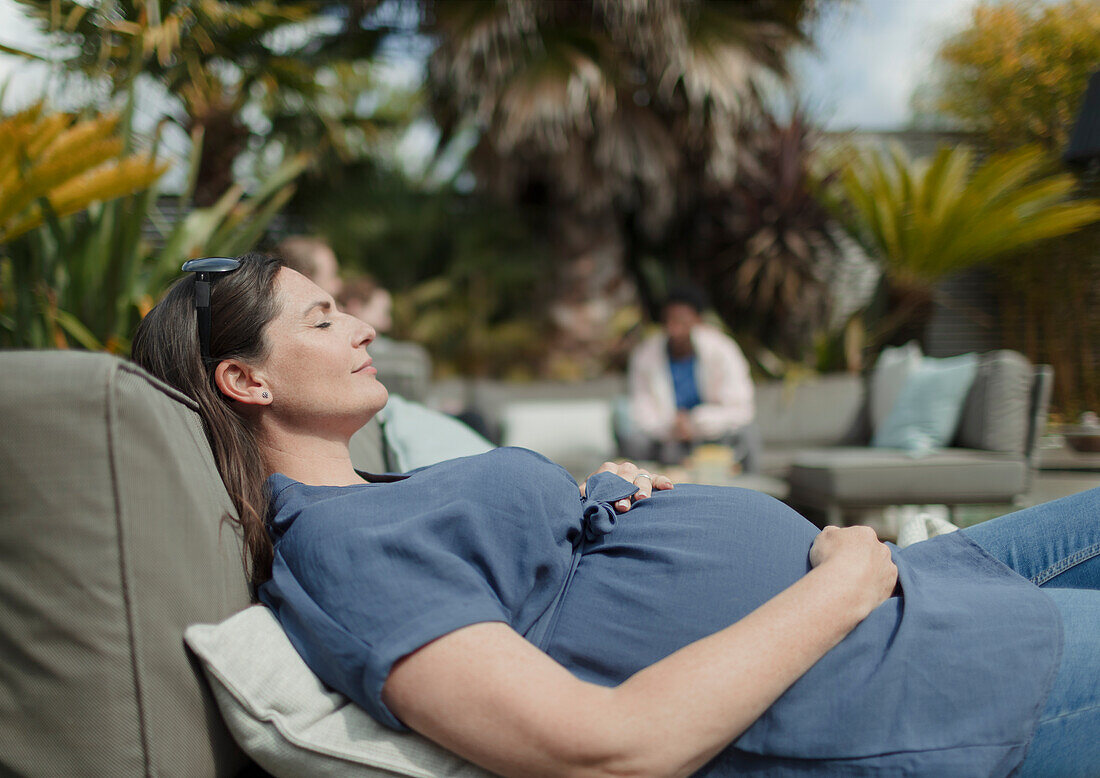 Pregnant woman relaxing on sunny patio lounge chair