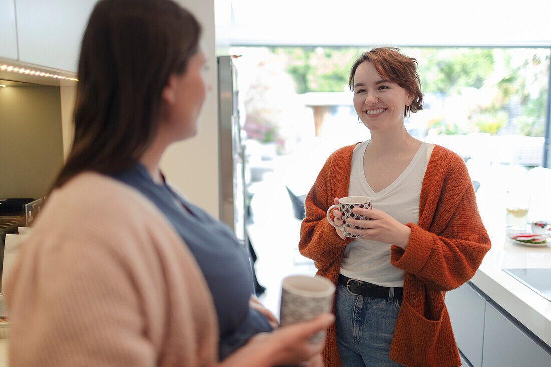 Young women friends talking and drinking coffee in kitchen