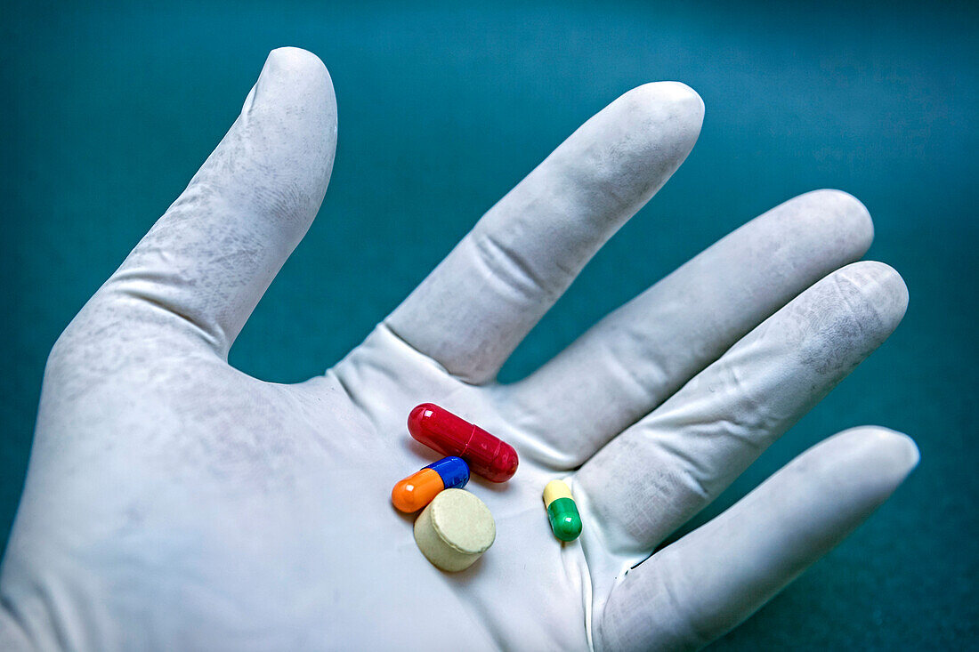 White gloved hand holding several pills