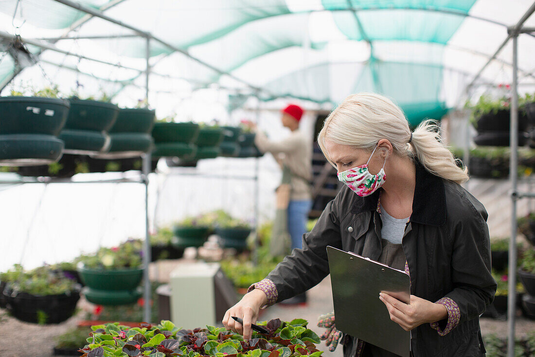 Female garden shop owner in face mask inspecting plants