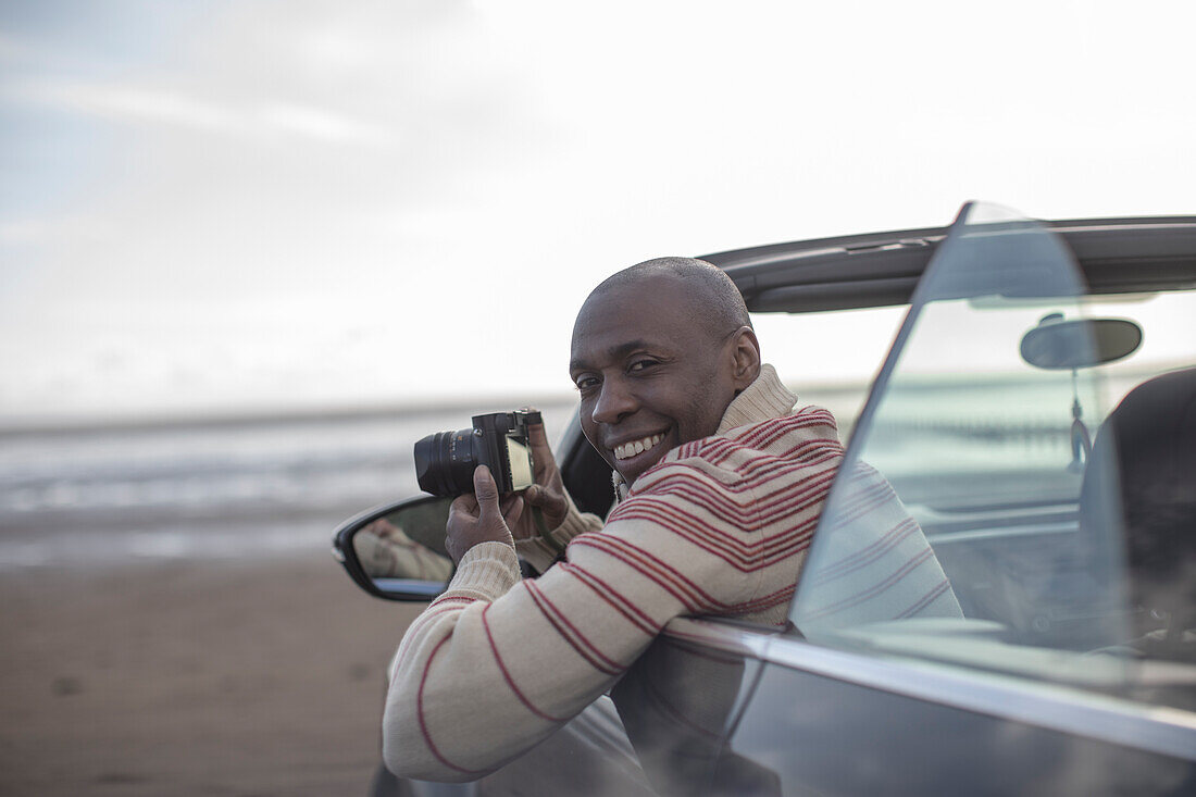 Happy man with digital camera in convertible on beach