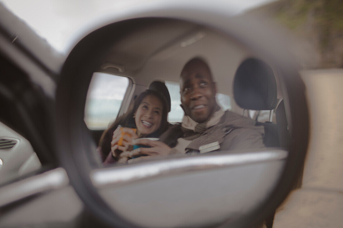 Reflection of happy couple drinking coffee in car mirror