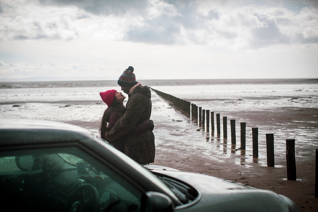 Affectionate couple hugging on wet winter beach