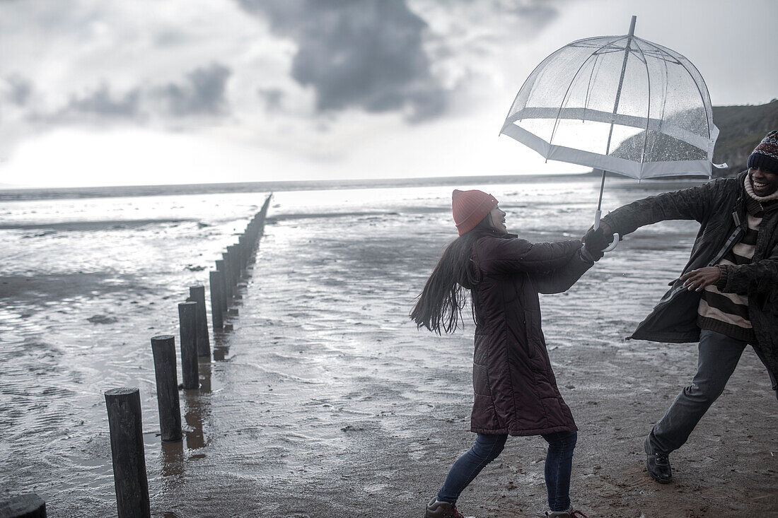 Playful couple with umbrella on wet winter ocean beach